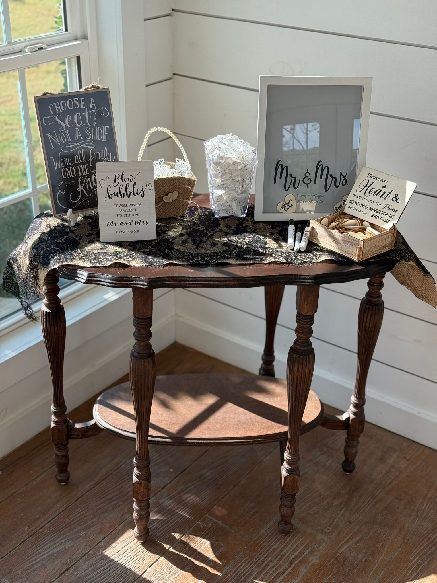 An antique table displays wedding decor: signs, a basket, and a box of favors.