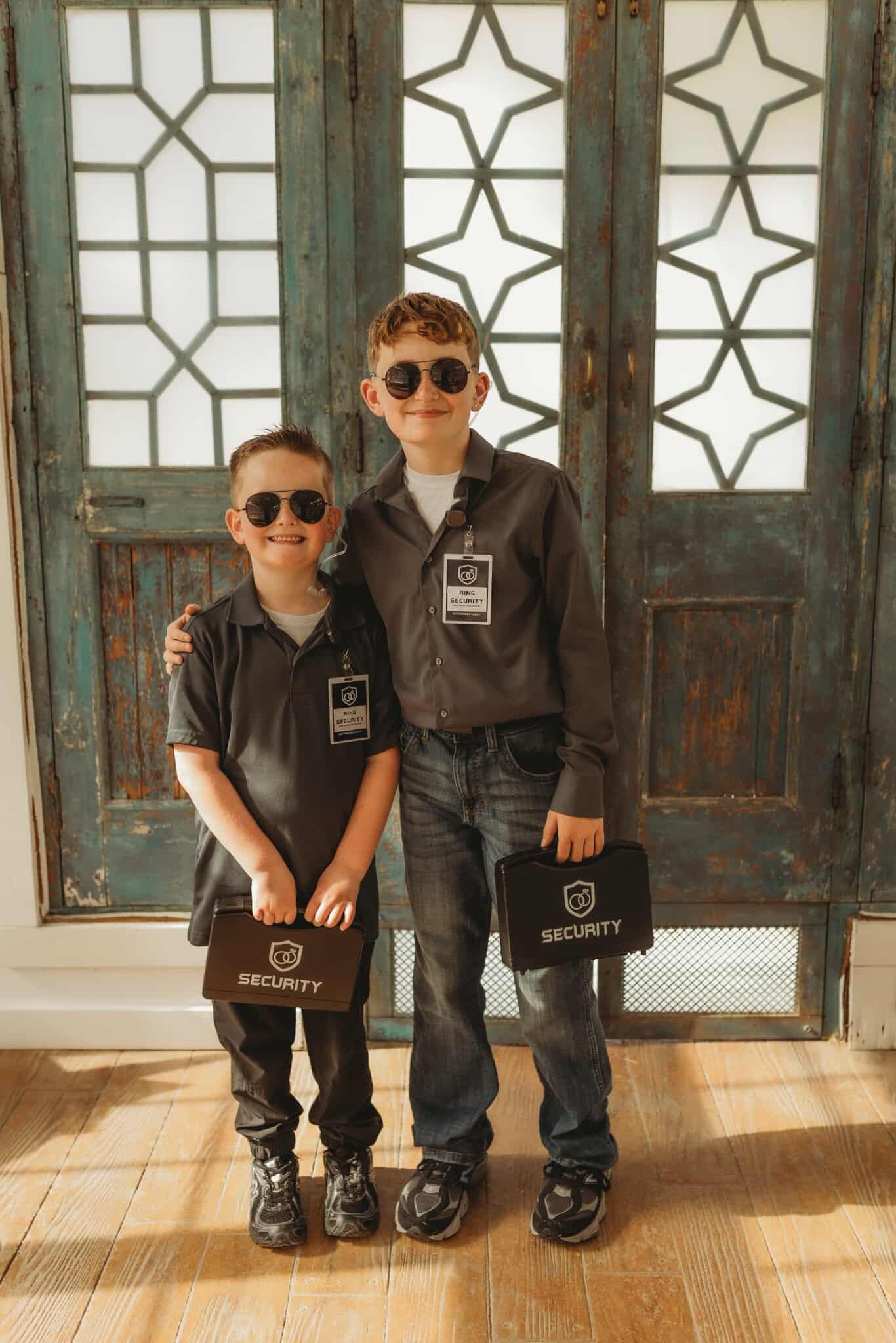 Two boys wearing sunglasses and uniforms, holding briefcases, standing in front of a patterned door.