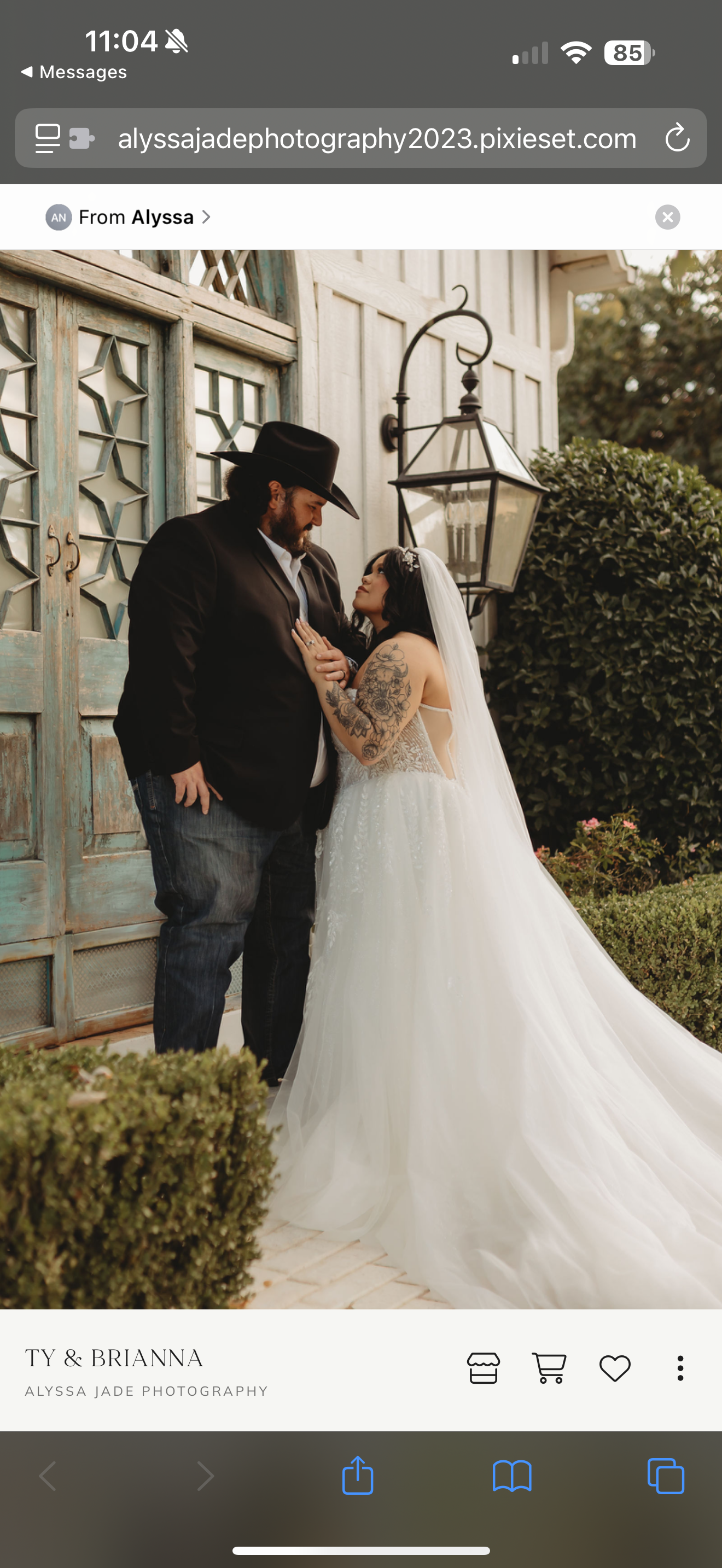 A couple in wedding attire stand near a building. The groom wears a hat and the bride a veil.