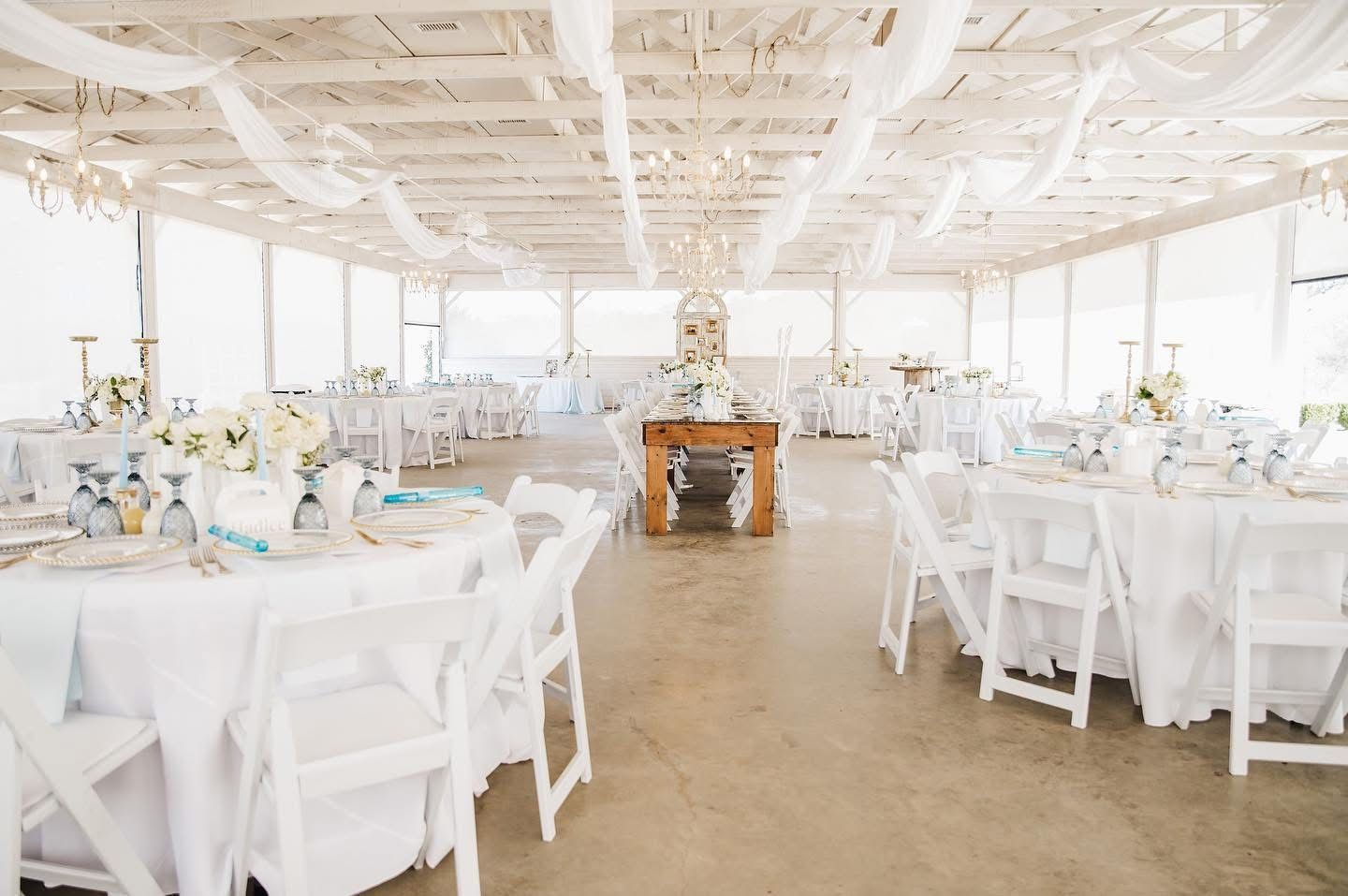 Wedding reception hall, tables set with white linens, draped ceiling, bright open space.