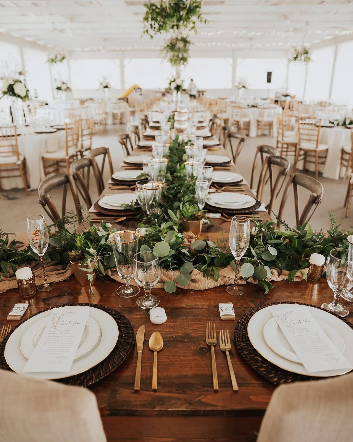 Wedding reception table setting with floral centerpiece and gold cutlery.