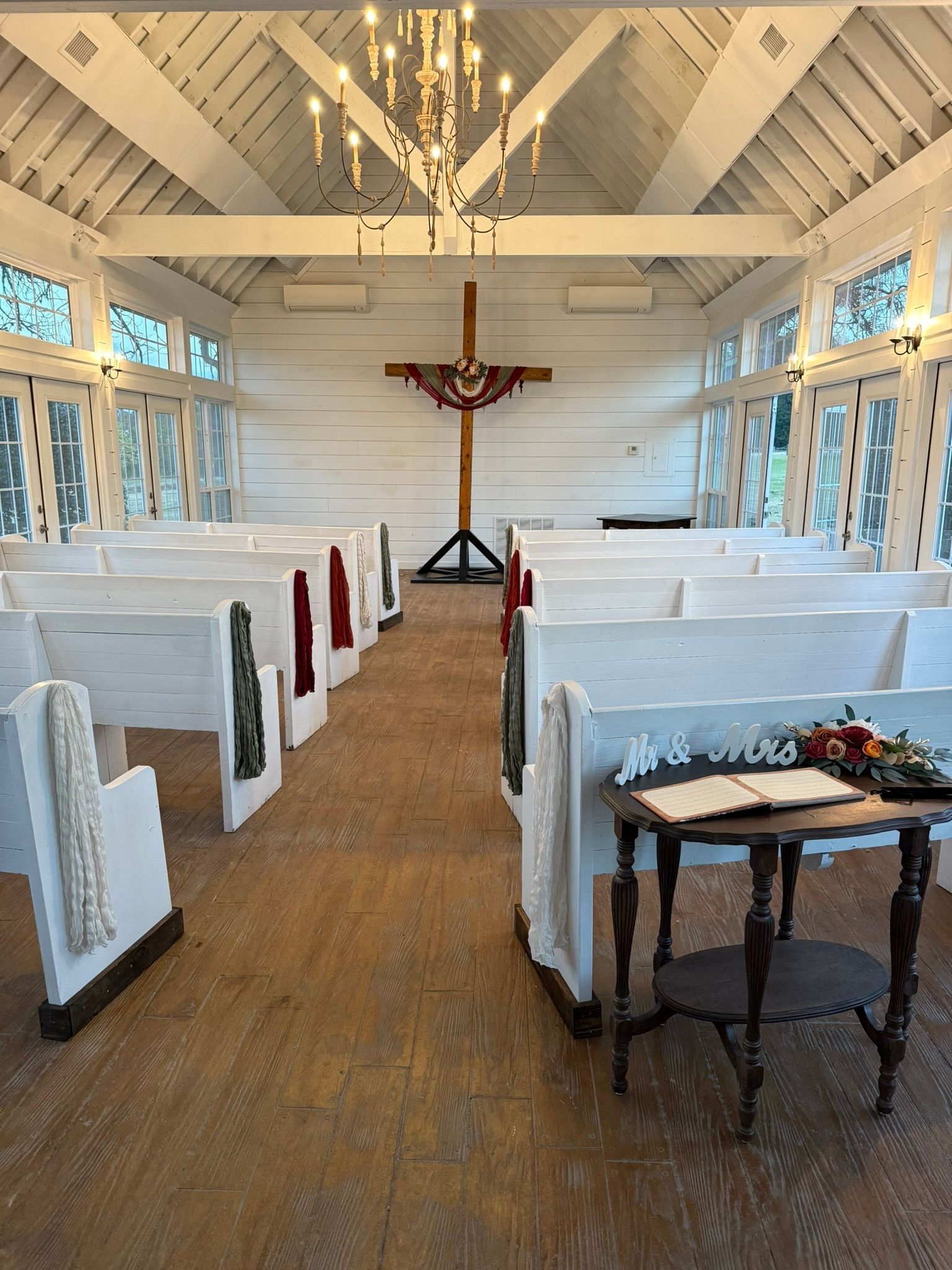 White chapel interior with cross, pews, and small table with flowers.