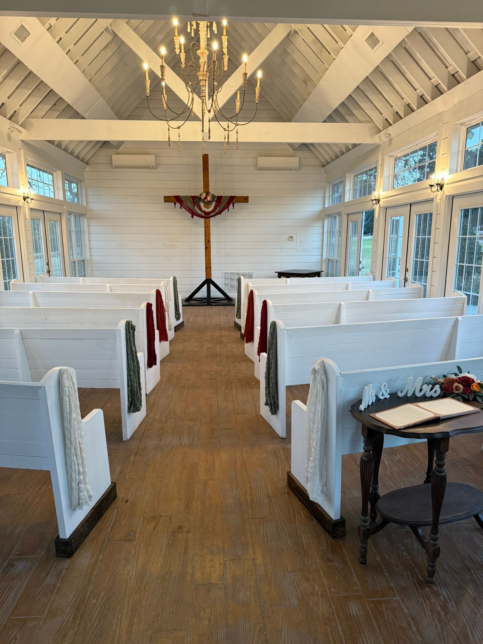 Interior of a white church with pews and a large crucifix. A small table holds flowers and a book.