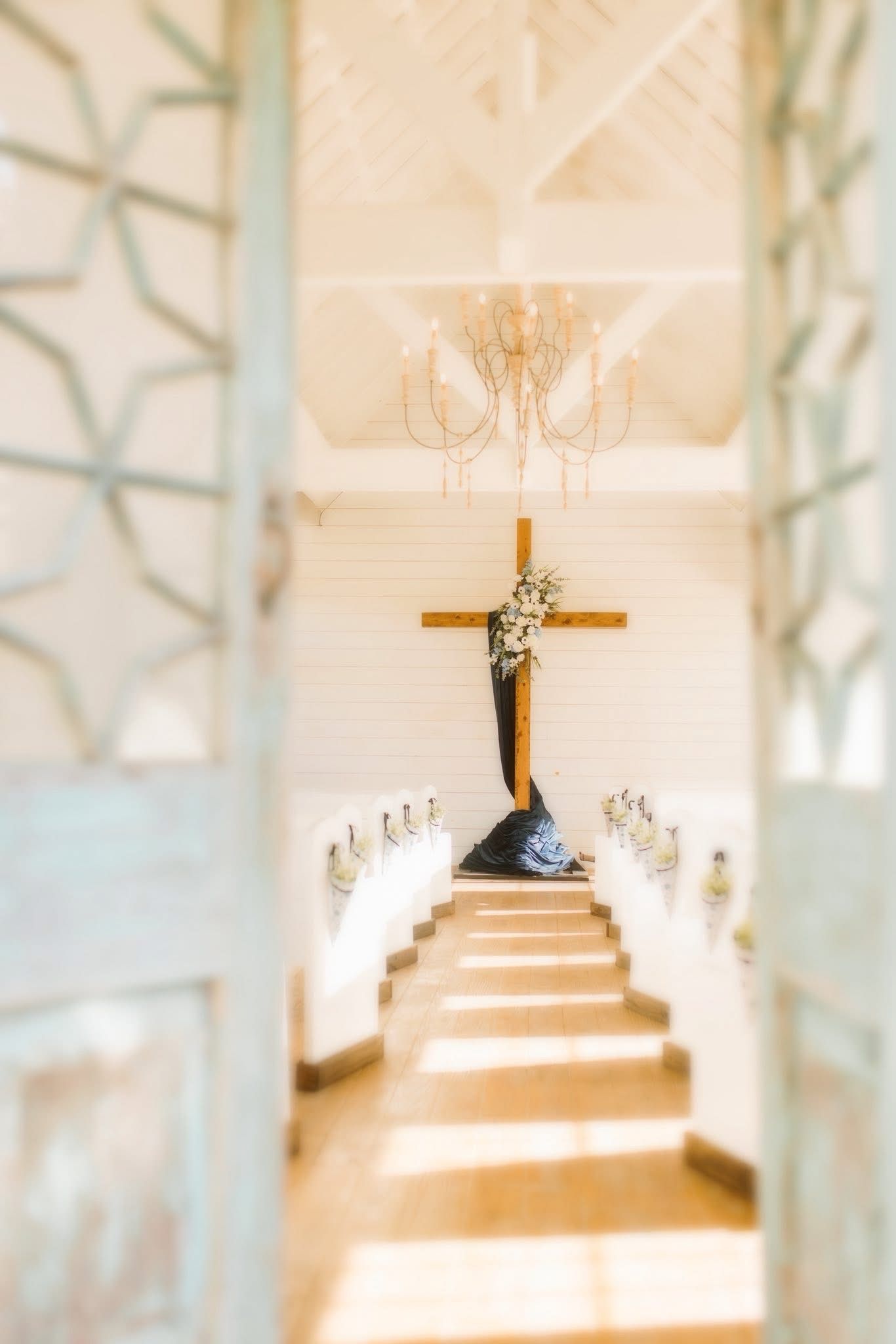 Wooden cross with a sculpted figure, centered at the end of a white-walled corridor.