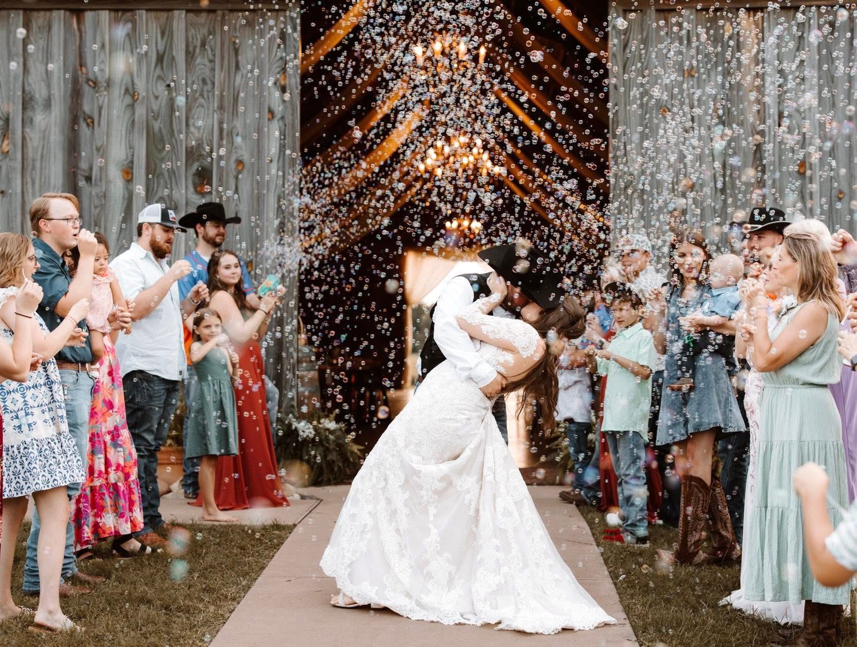 Newlyweds kiss under confetti shower as guests celebrate outside a barn.