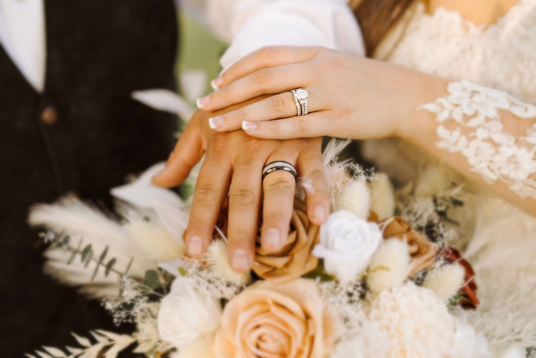 Close-up of hands with wedding rings on top of a bouquet of flowers.