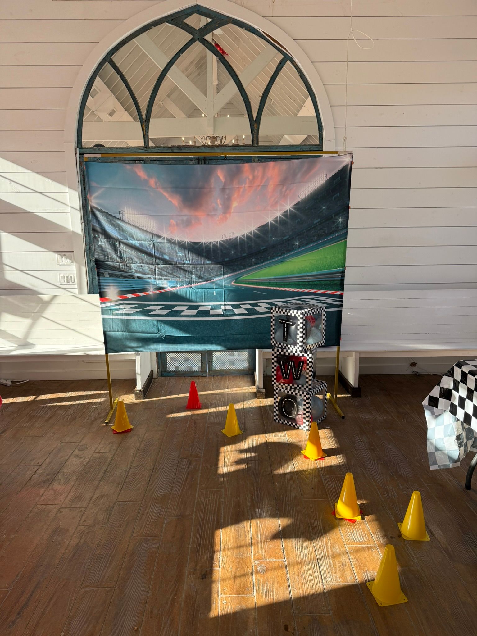 Race car track setup with cones, backdrop of a stadium, and a checkered flag; inside a room with arched window.