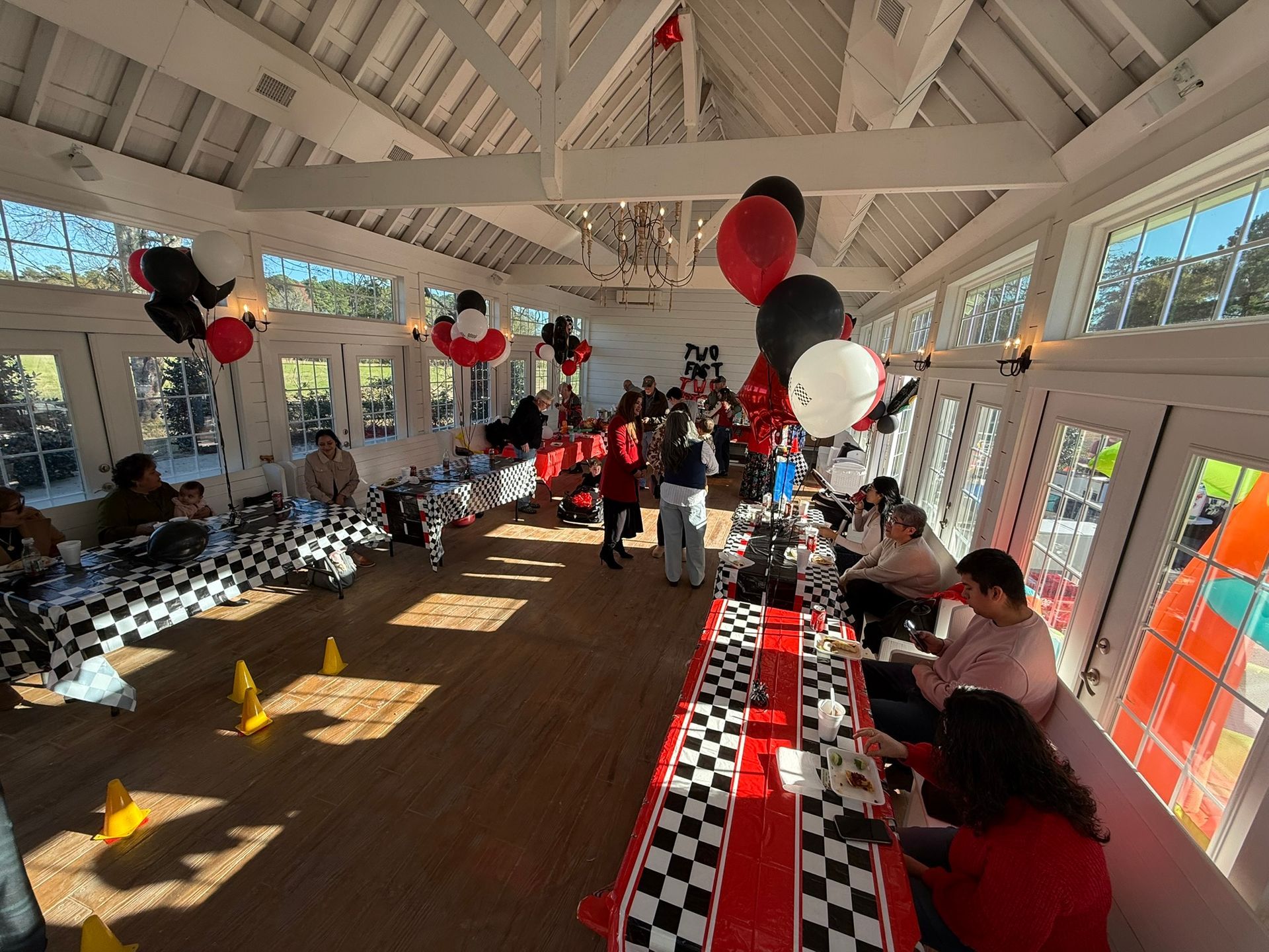 Party room decorated with race car theme; checkered tables, red accents, balloons, people.