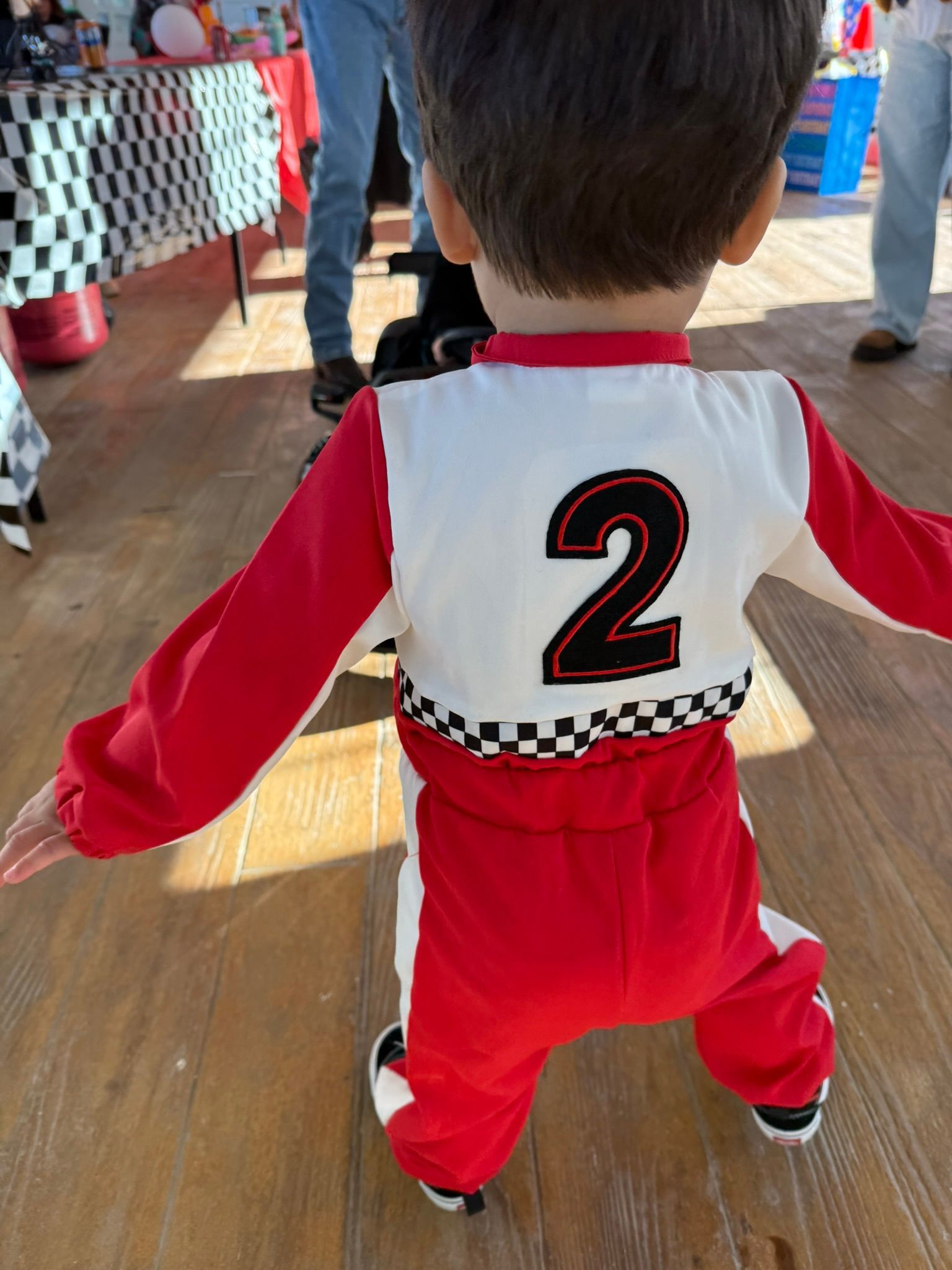 Child in red and white racing suit, number 2 on back, arms outstretched.