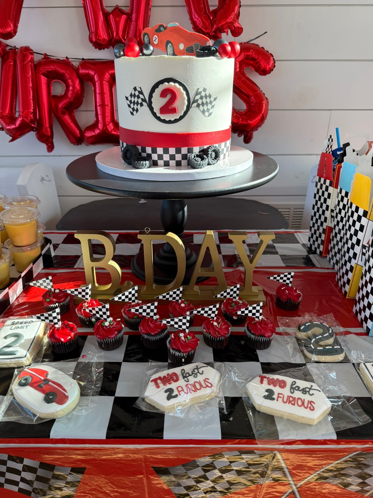 Birthday cake and treats on a checkered table. Red and gold decorations, racing theme.