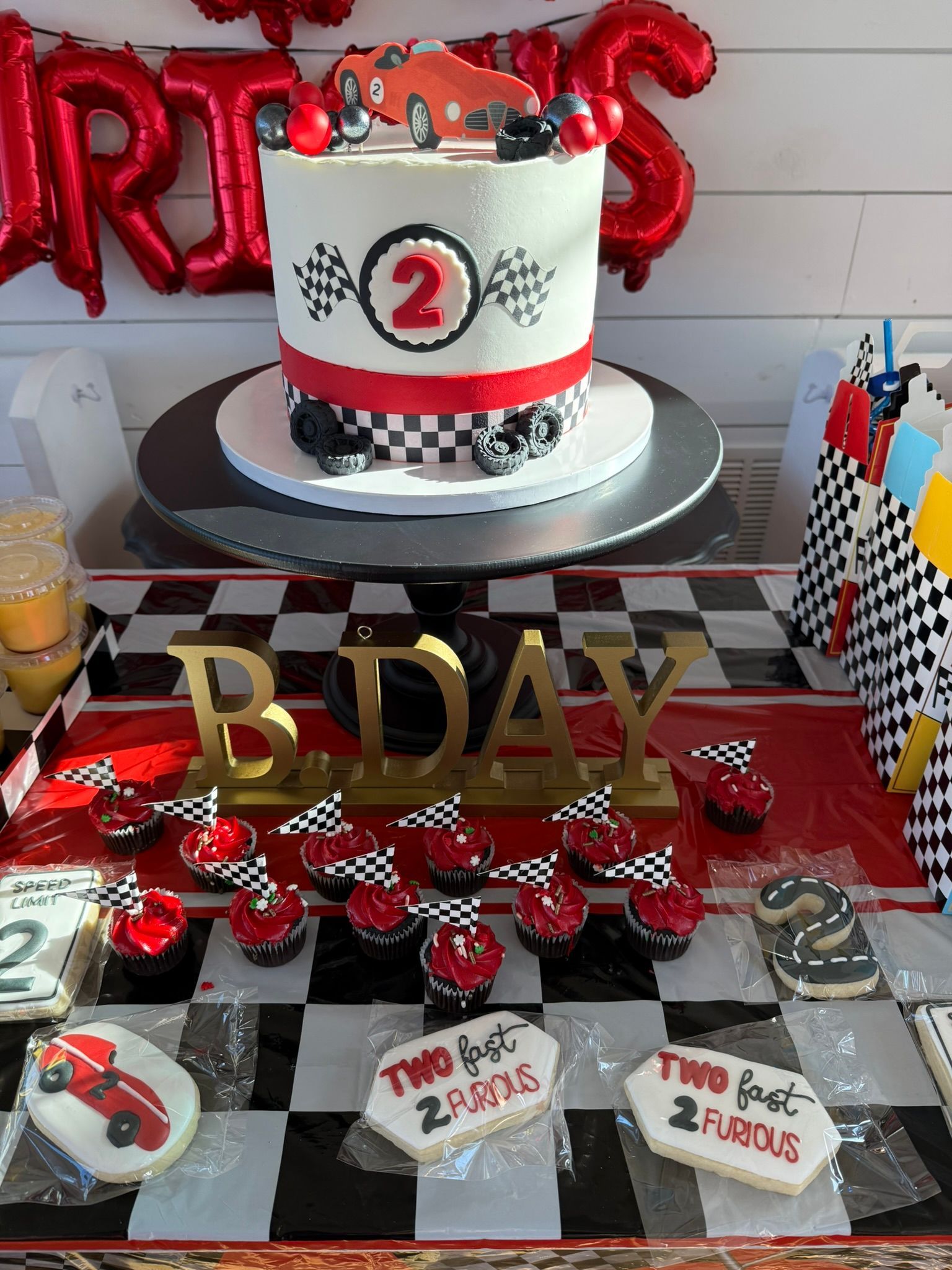Race car themed 2nd birthday party: cake with car on top, cupcakes, cookies, and decorations.
