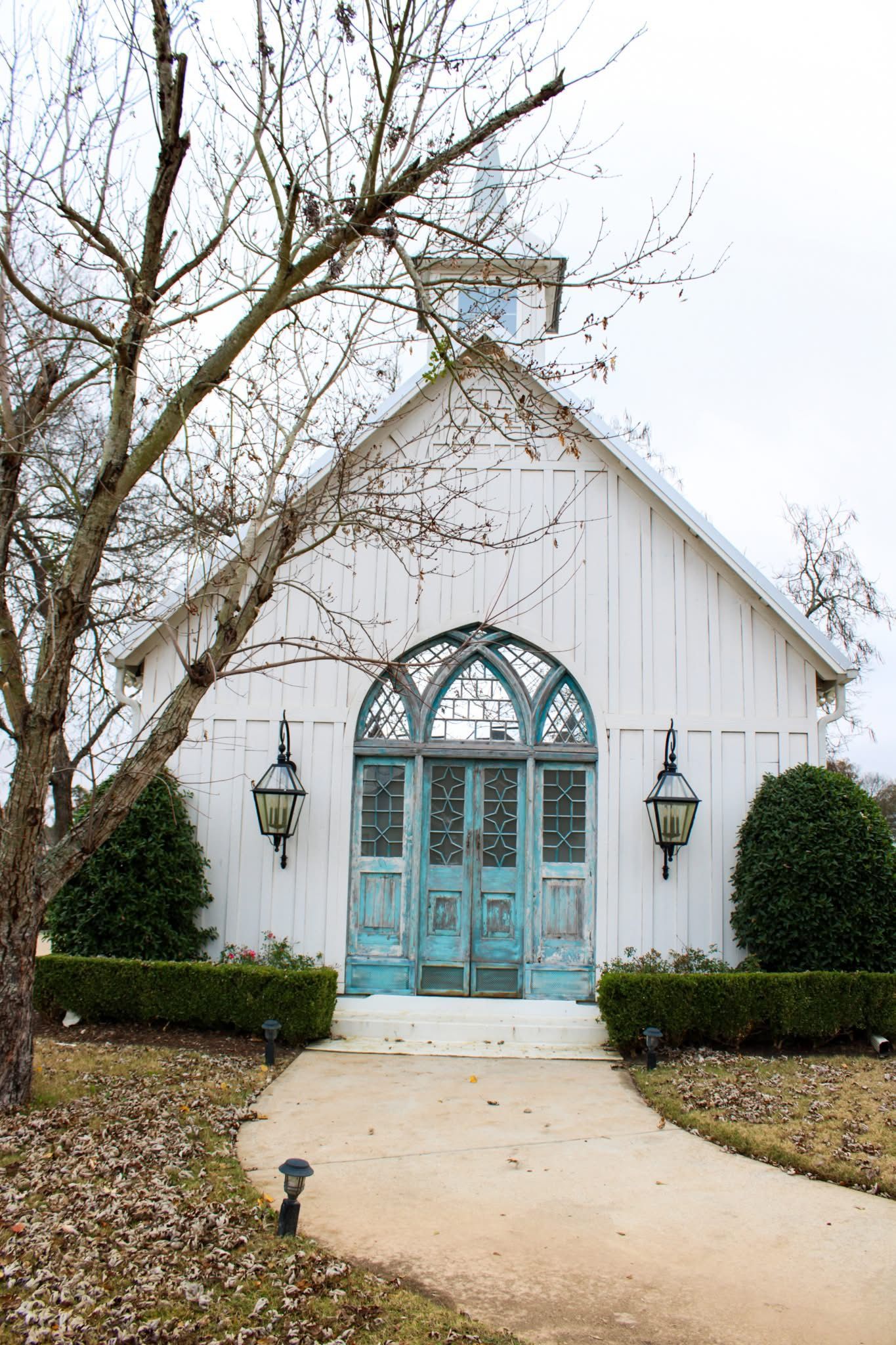 White chapel with turquoise doors, arched window, and lanterns. Path leads to the entrance.