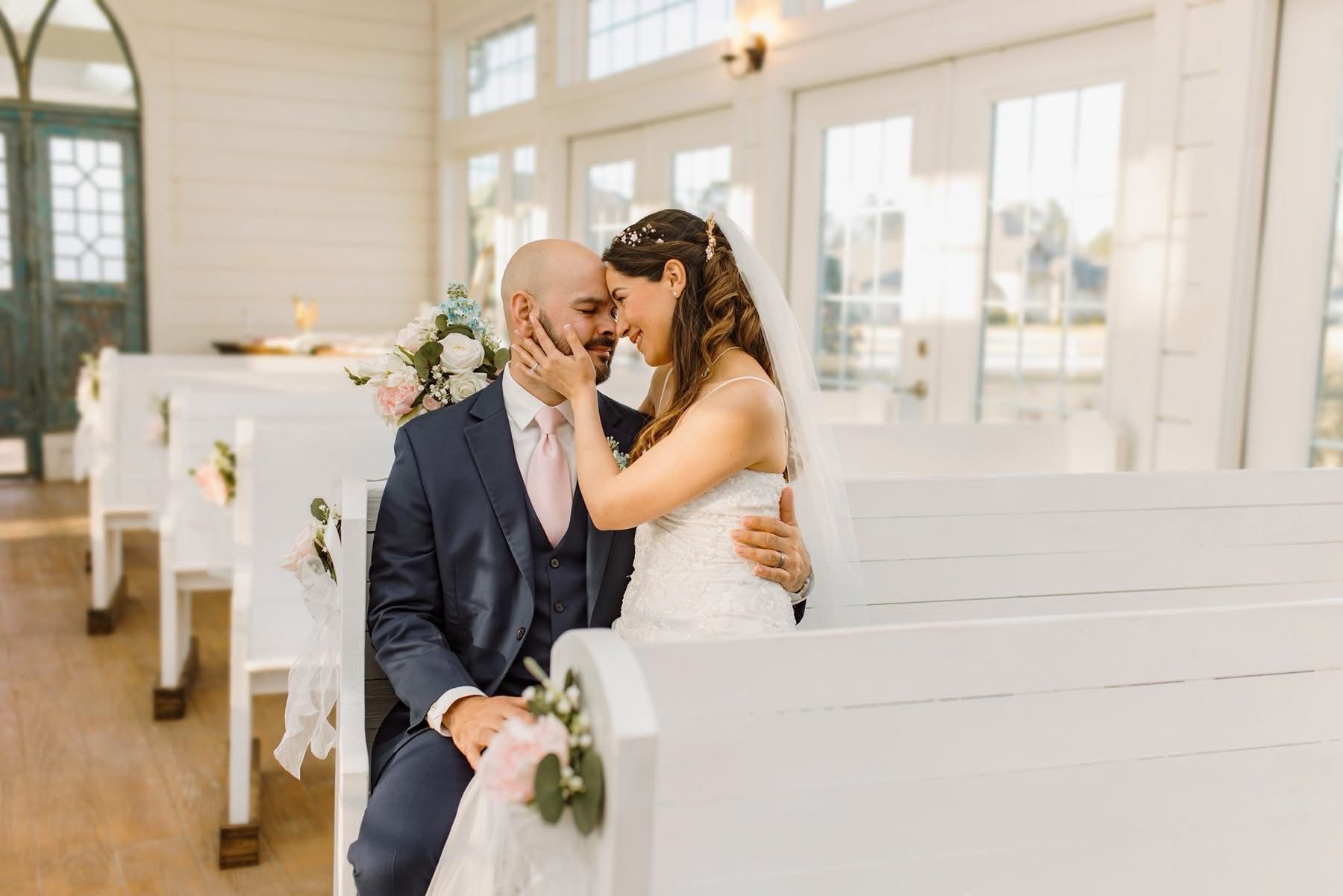 Bride and groom embracing in a white chapel, adorned with flowers, during their wedding.