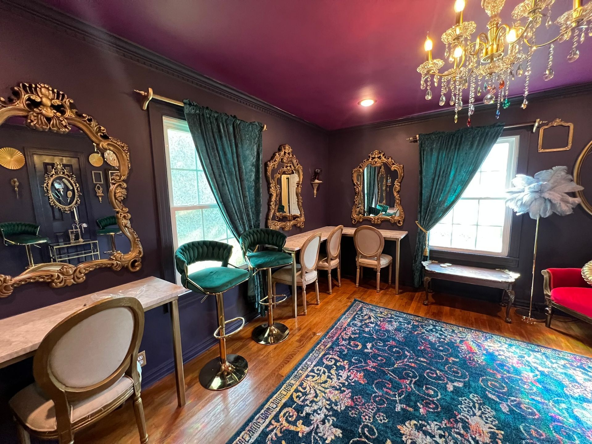 Elegant, dark-walled room with gold mirrors, teal curtains, and chandelier. Includes velvet chairs and a patterned rug.