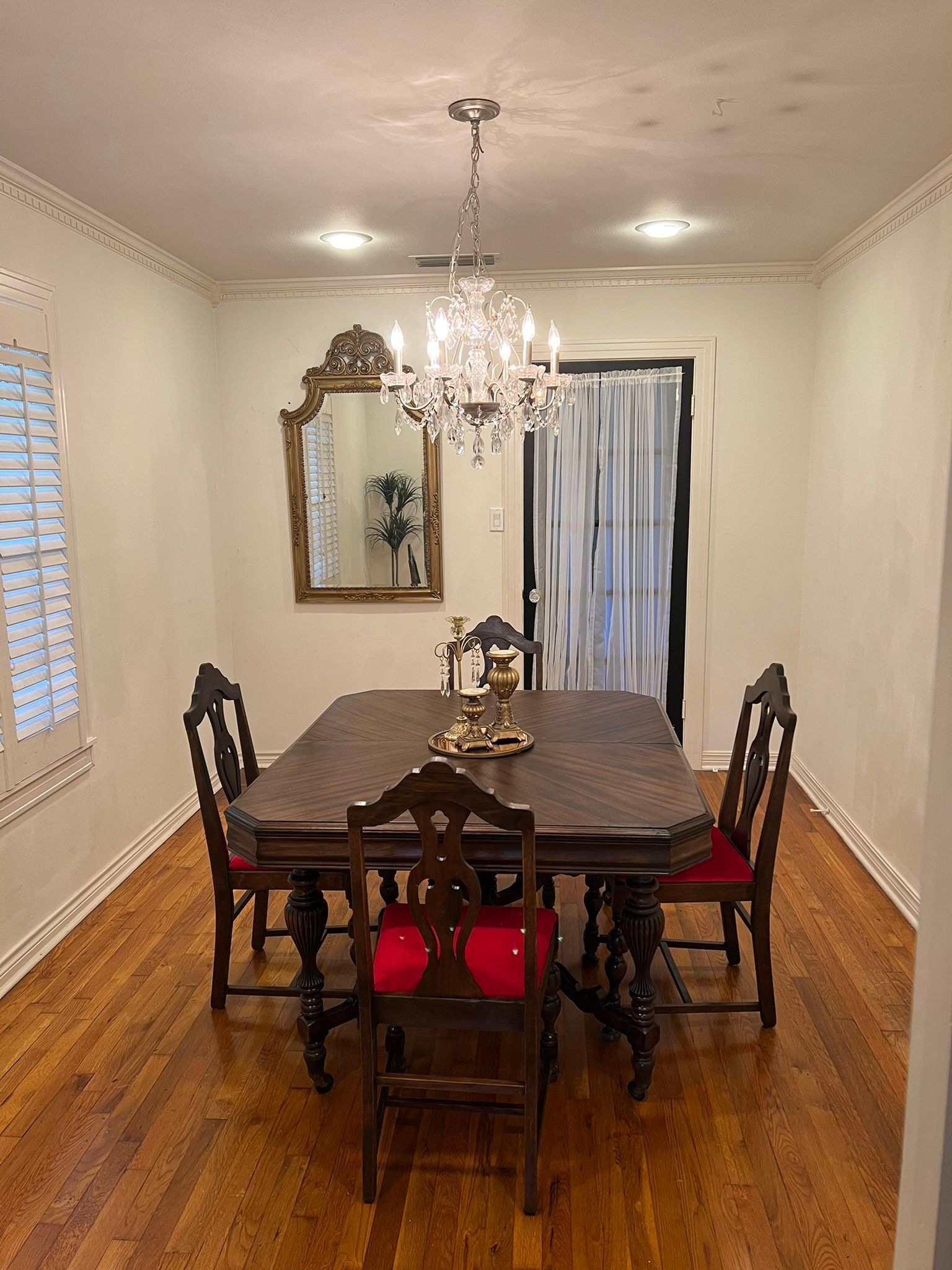 Dining room with wooden table, chairs, mirror, chandelier, and hardwood floors.