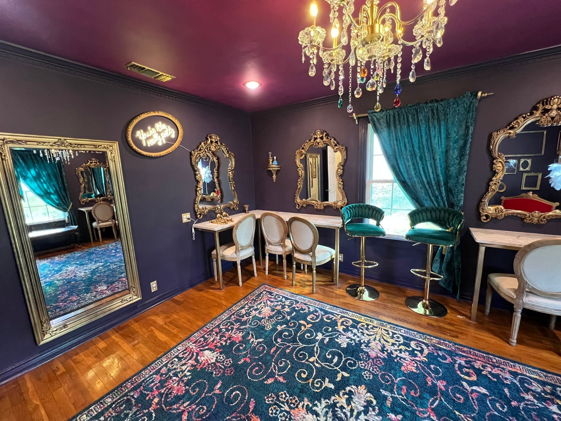 Purple room with ornate mirrors, chandelier, teal curtains, and a patterned rug.