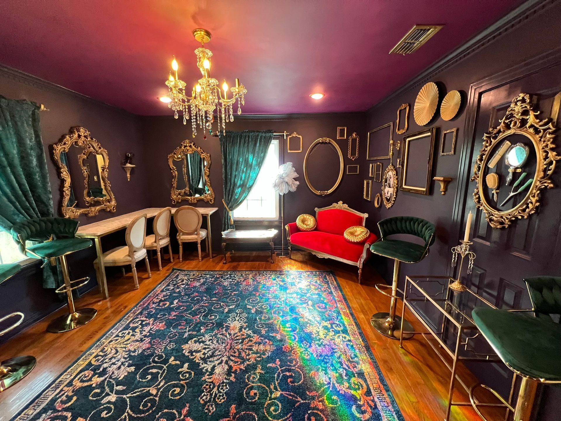 Elegant, dark room with a red couch, ornate mirrors, a chandelier, and a colorful rug.