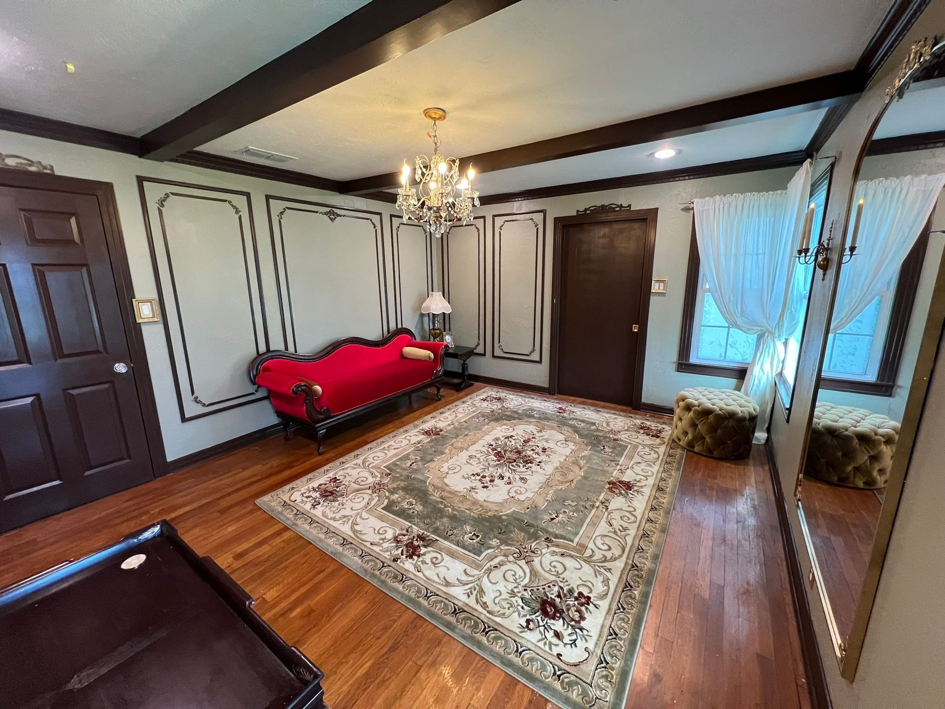 Luxurious room with red sofa, ornate rug, chandelier, and tall mirror.