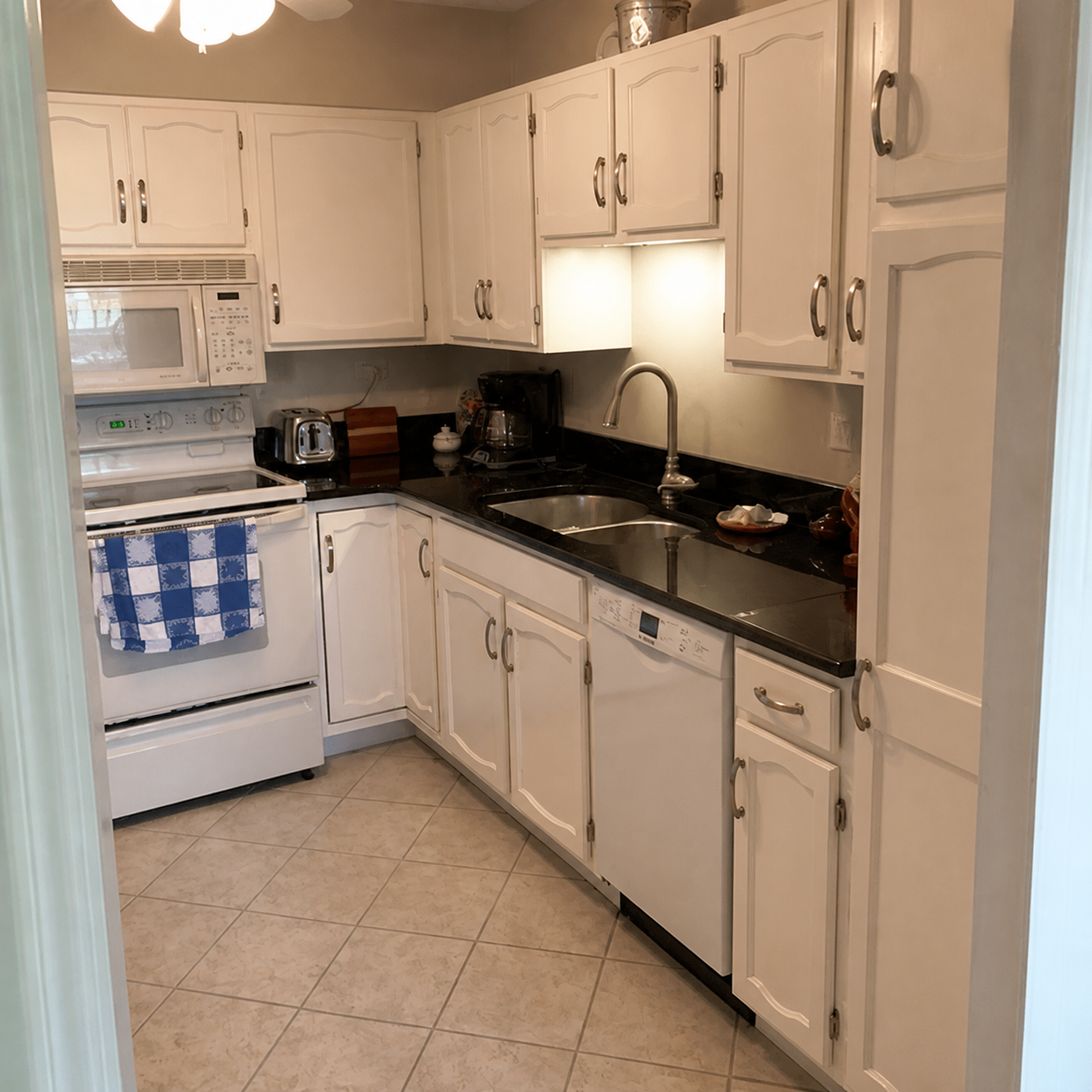 Small white kitchen with black countertop, white cabinets, and tiled floor.