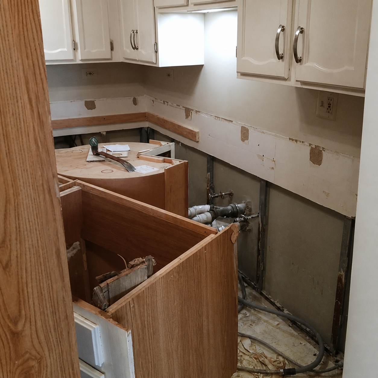 Partially demolished kitchen with removed cabinets, exposed wall, and debris on the floor