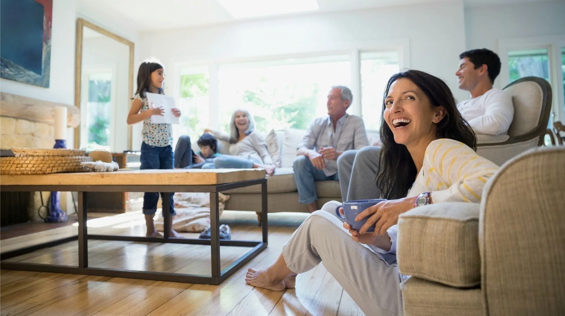 People relaxing in a bright living room, with one smiling in the foreground and others seated behind.
