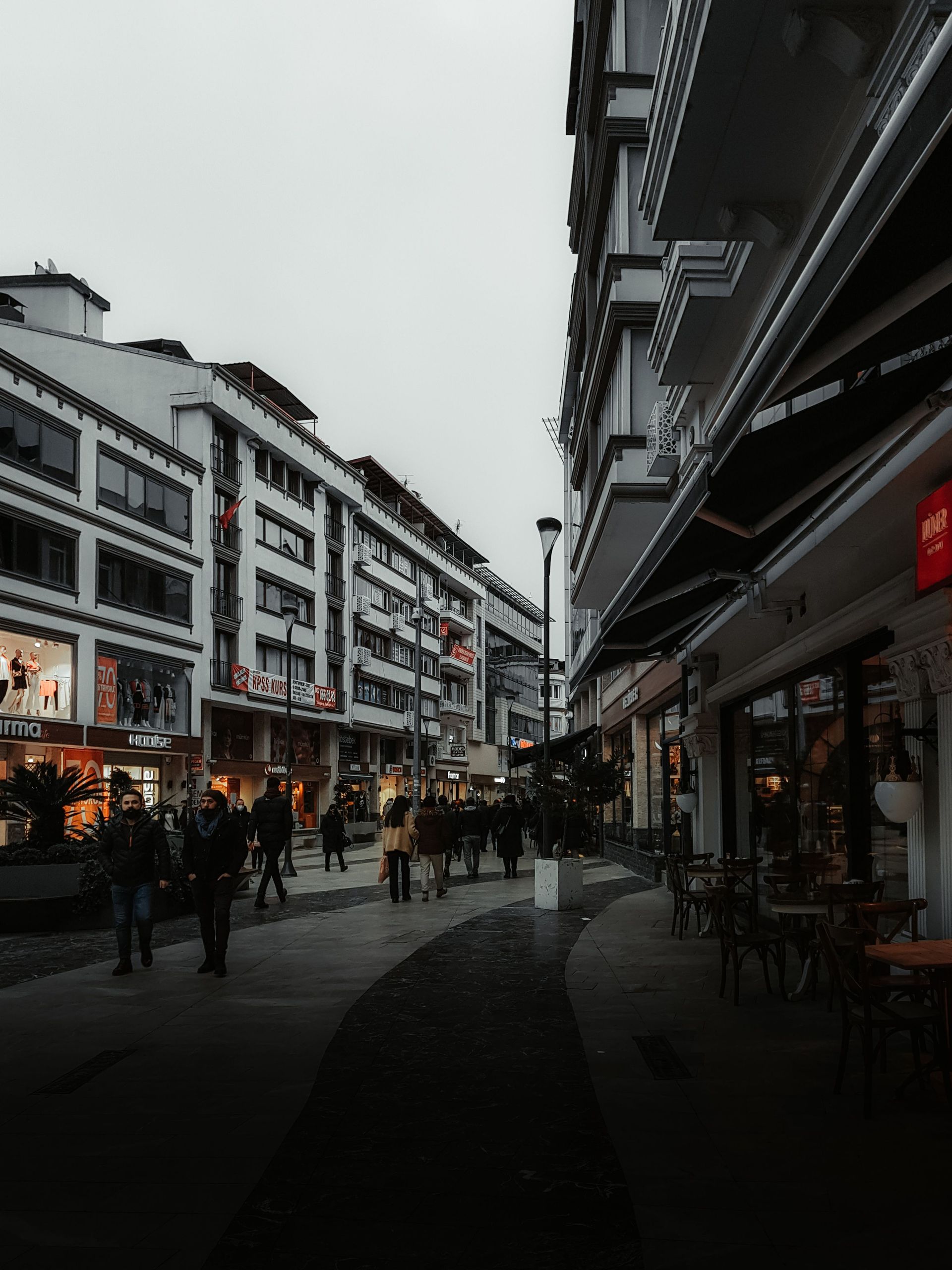 Busy pedestrian street lined with shops and buildings under a gray sky