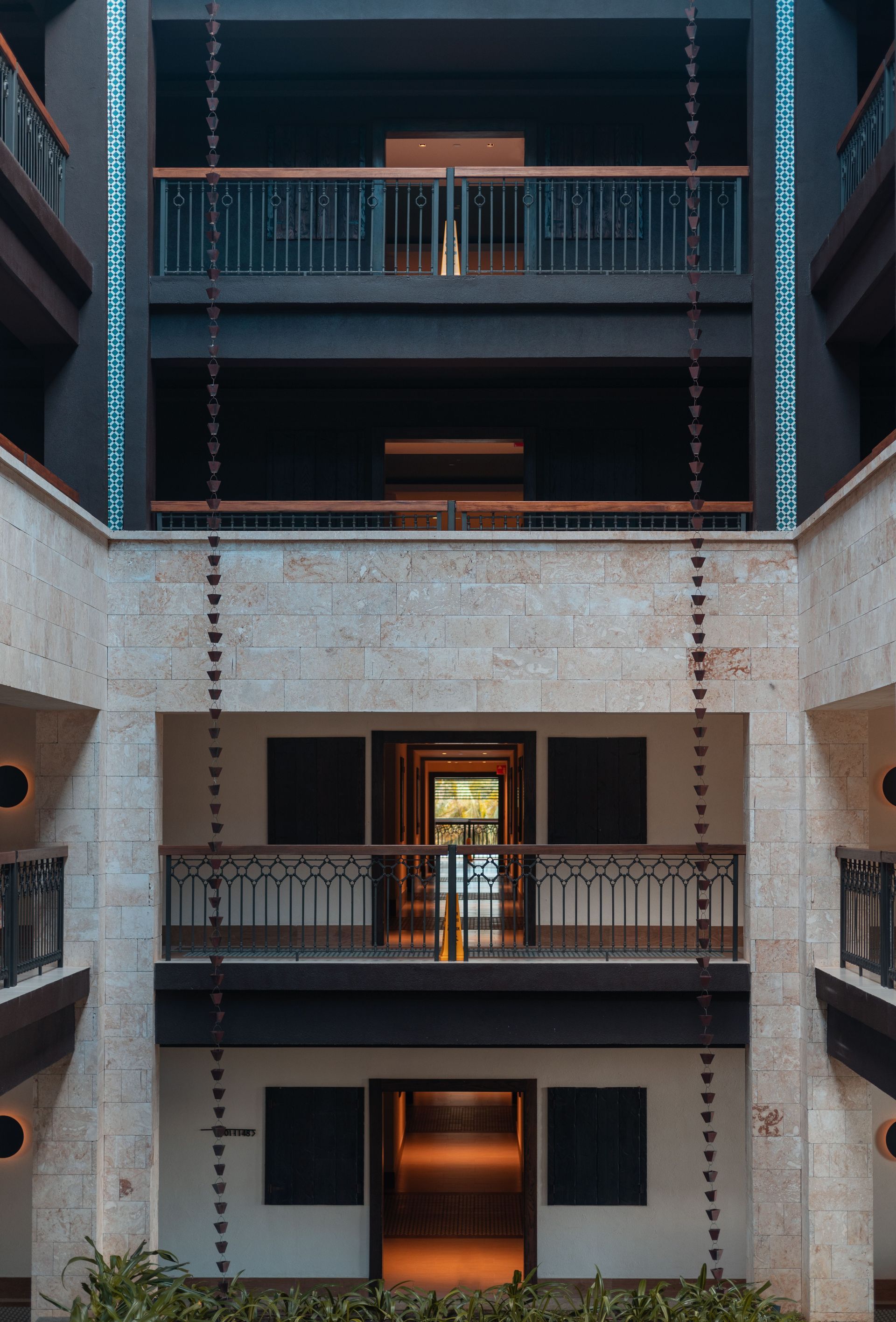 Interior atrium with three stories, dark railings, hanging chains, and doors centered on each level