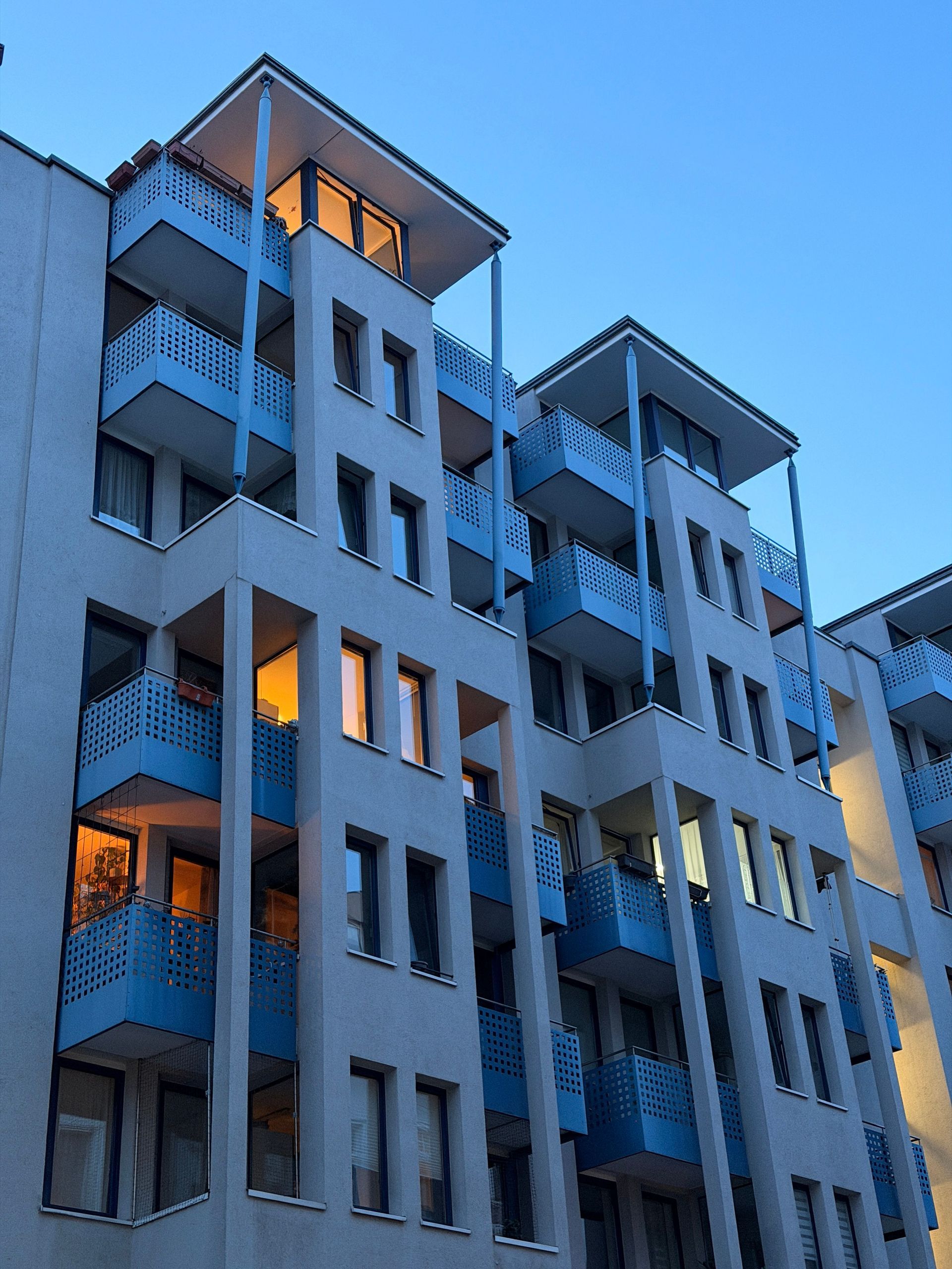 Blue apartment building at dusk with lit windows and balconies