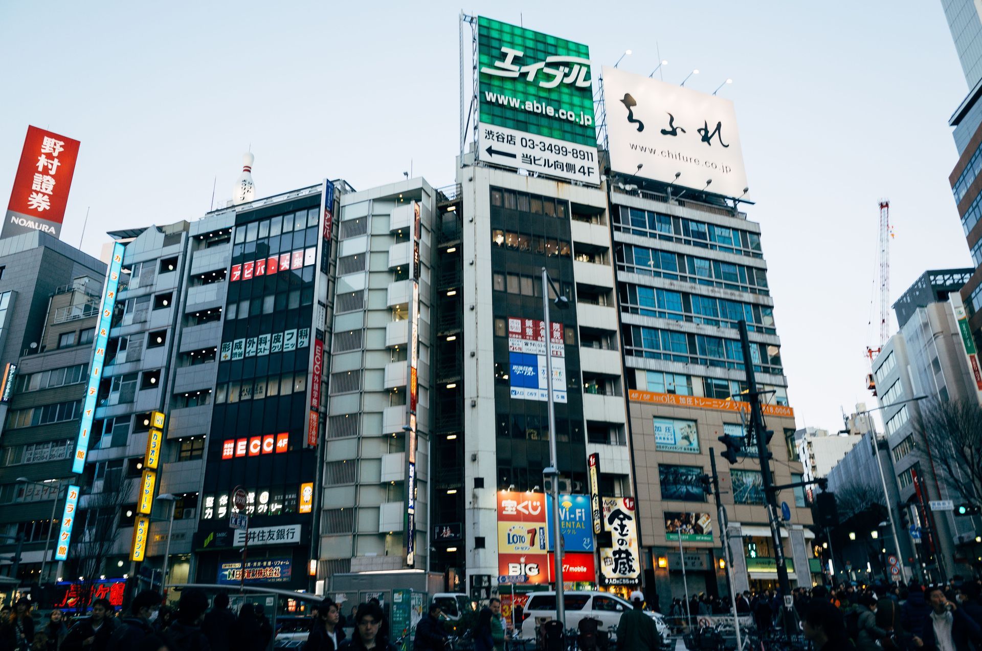 Busy urban street with tall buildings, colorful signs, and a crowd at an intersection.