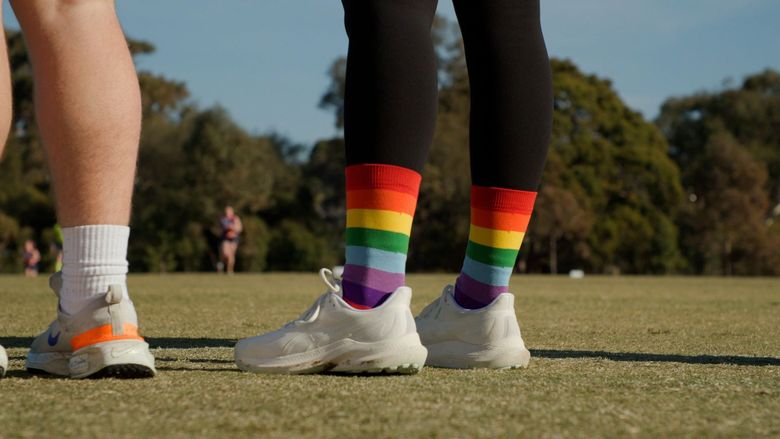 Two people wearing athletic shoes and rainbow socks stand on grass at a park.