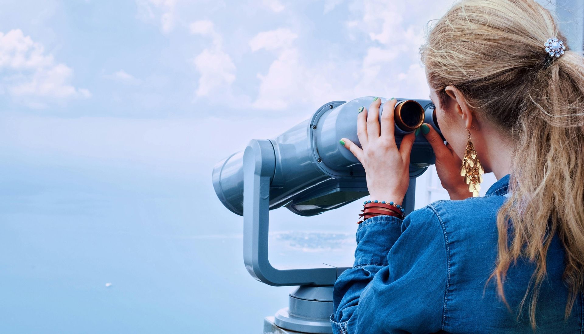 Person looking through a coin-operated binocular viewer over a calm blue seascape