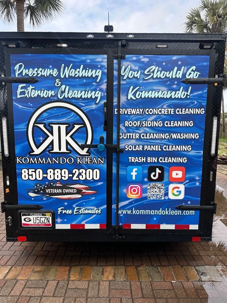 Rear of a black trailer with blue and white Kommando logo and services listing: power washing, cleaning, contact info.