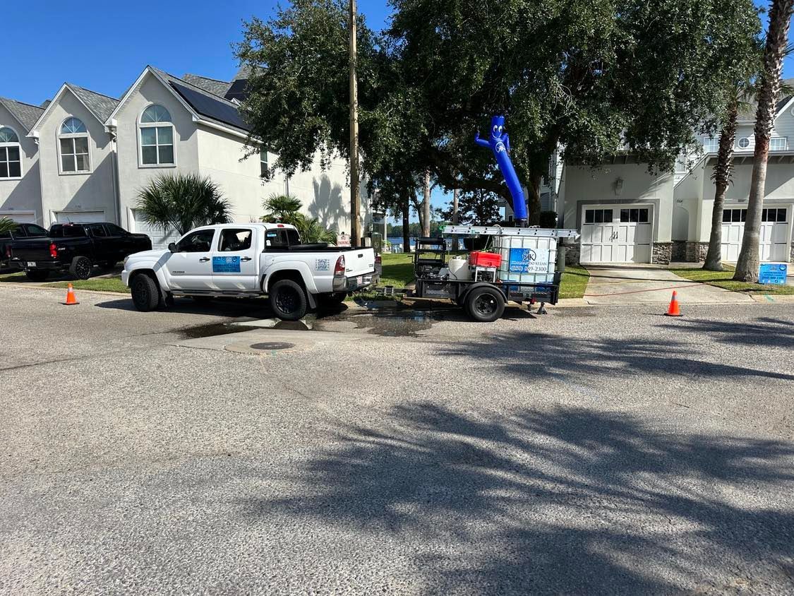 White truck and trailer parked on a driveway near two houses, orange cones.