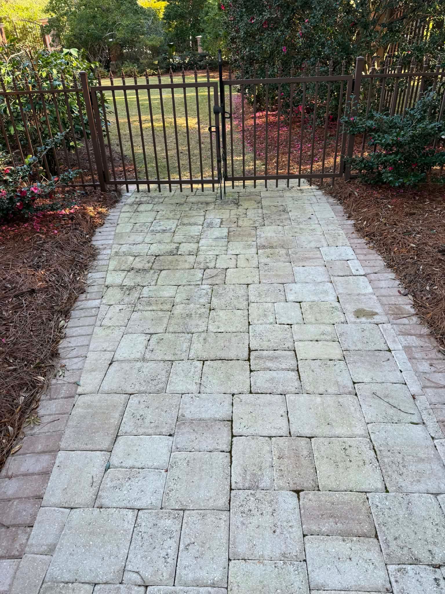 Weathered paver walkway near a metal garden gate before professional sealing