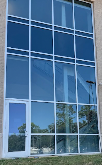 Large glass windows and a door reflecting trees and sky, on a light-colored building.