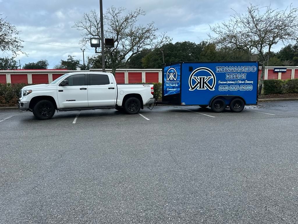 White pickup truck towing a blue trailer with business logo in a parking lot.
