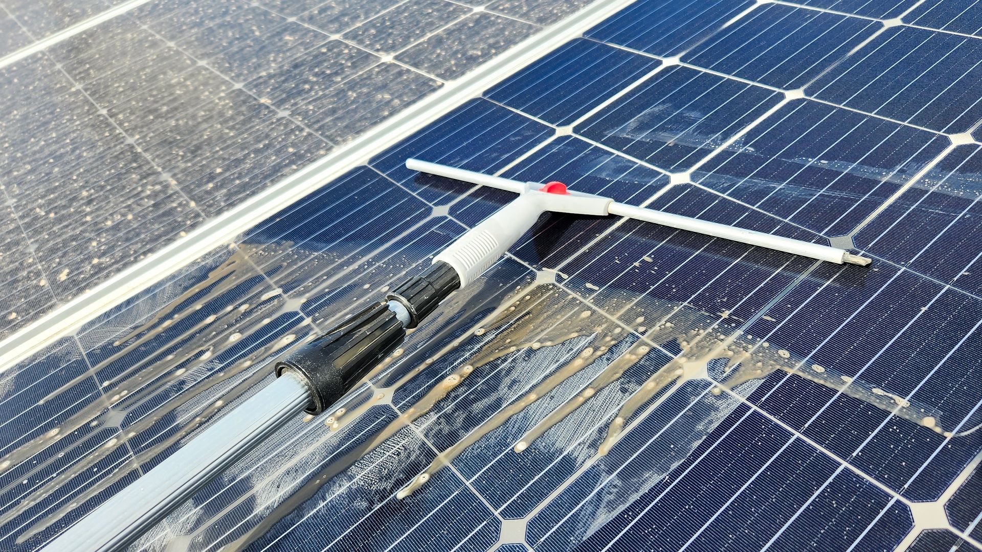 Cleaning solar panels with a long-handled brush; panels are dusty.
