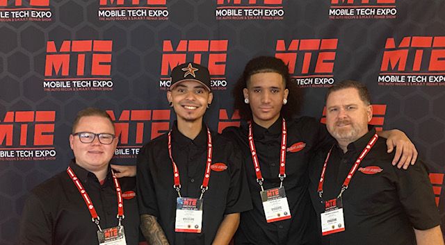 Four people pose in front of a Mobile Tech Expo backdrop, smiling with lanyards around their necks.