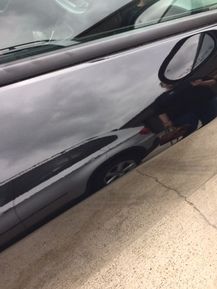 Black car door reflecting a silver car and cloudy sky.