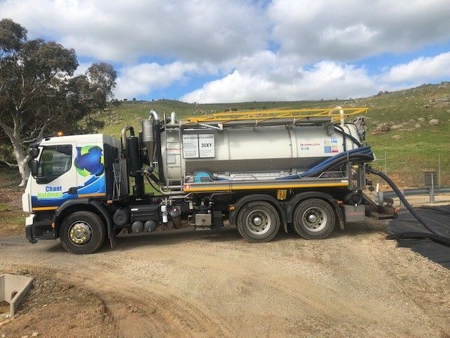 A vacuum truck is parked on the side of a dirt road.