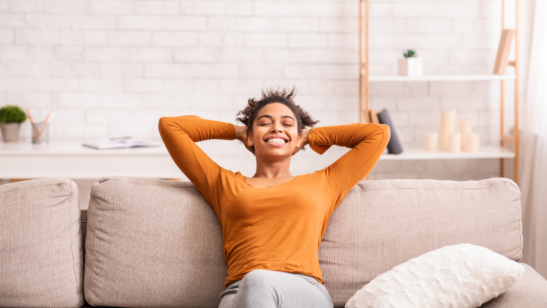 Une femme est assise sur un canapé avec ses mains derrière sa tête et sourit.