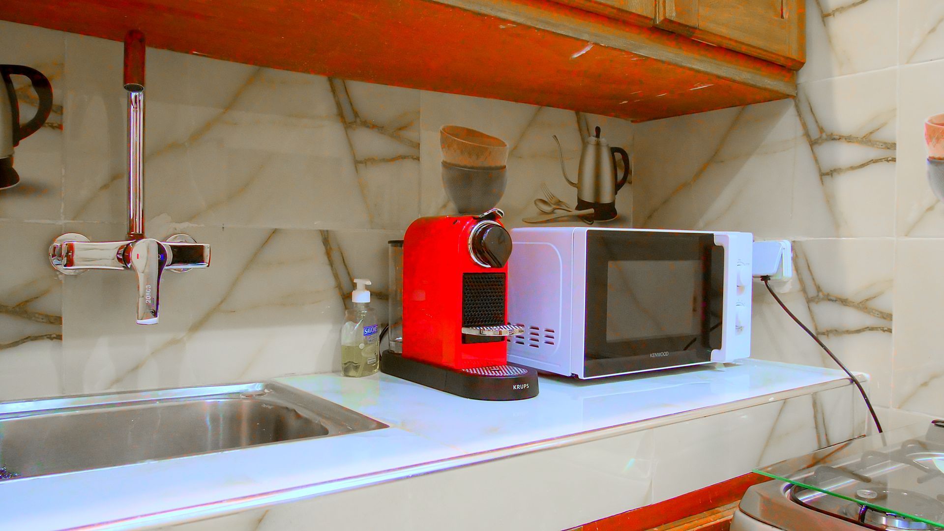 Une cuisine avec un évier, un micro-onde, une cafetière et un mixeur.