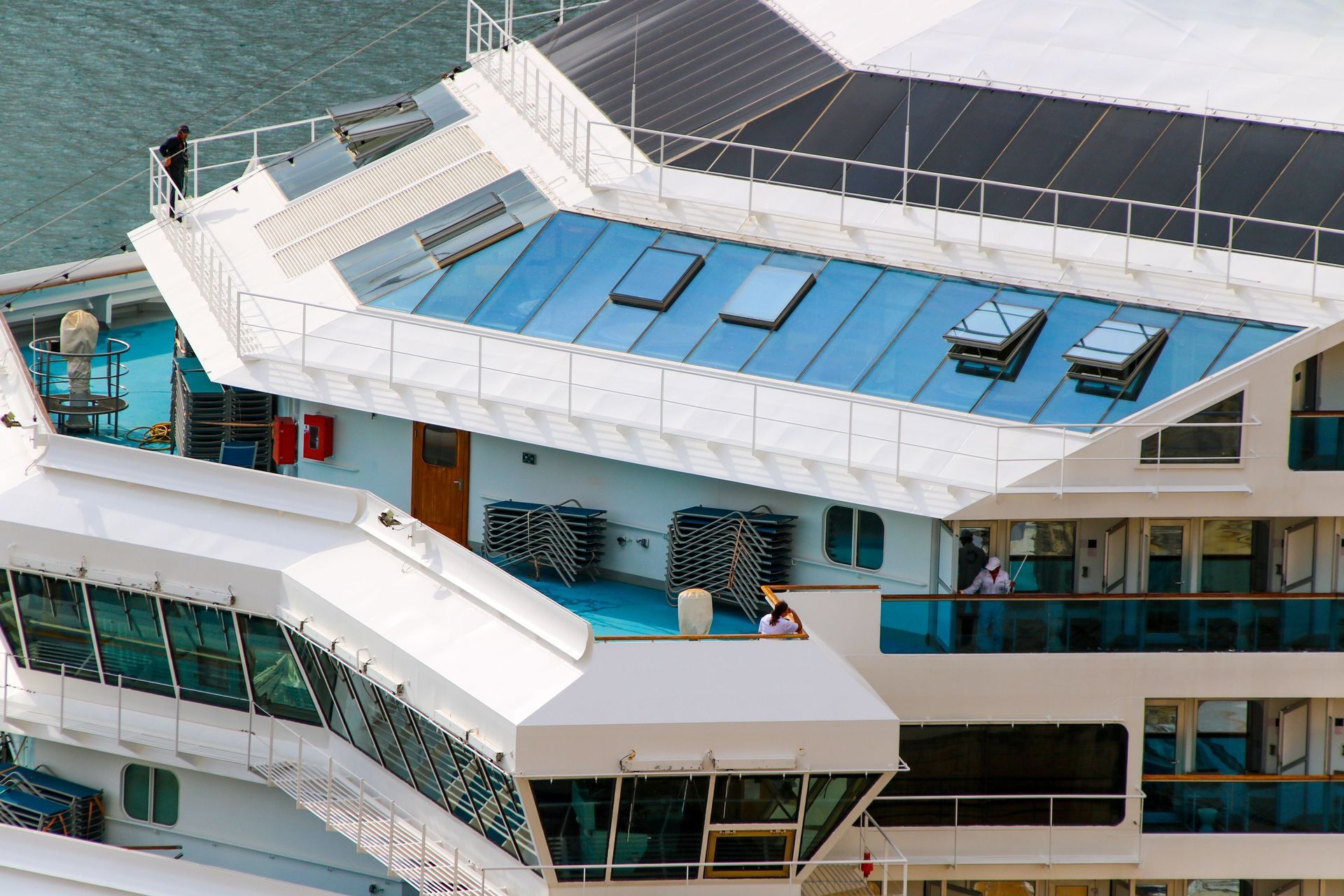 Top deck of a cruise ship with blue sun loungers and white railings overlooking the sea.