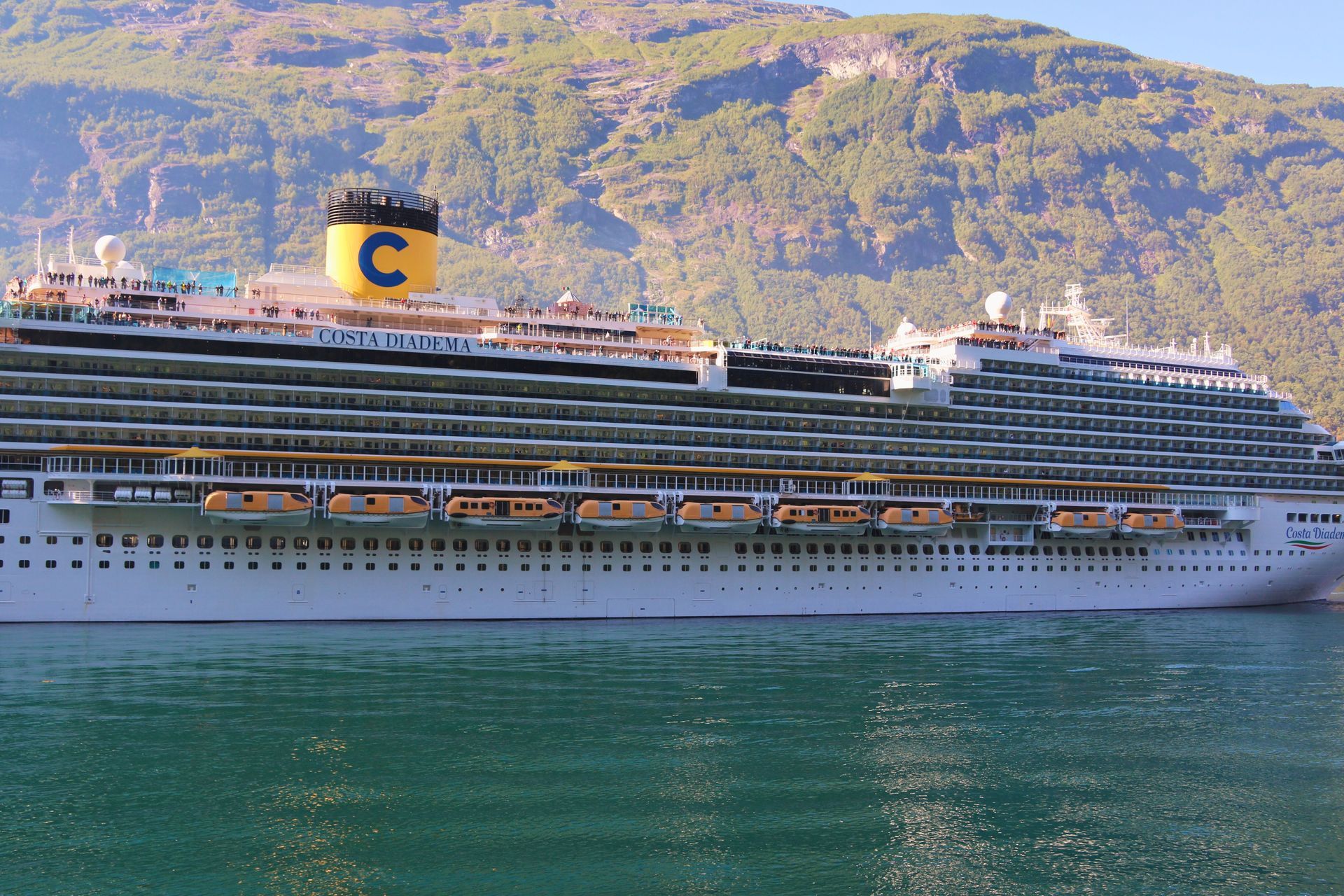 Large white cruise ship sailing on green water with mountains in the background