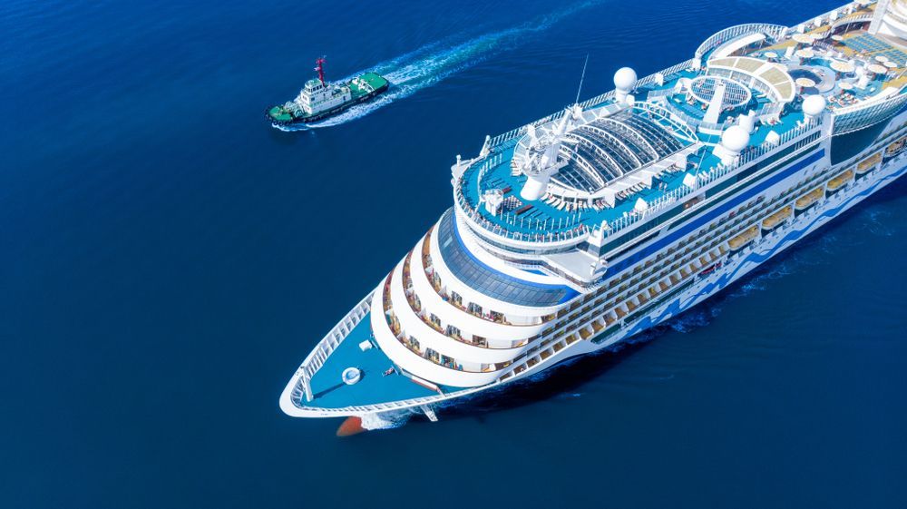 Two cruise ships sailing on deep blue water, one large white ship in the foreground and a smaller one behind.