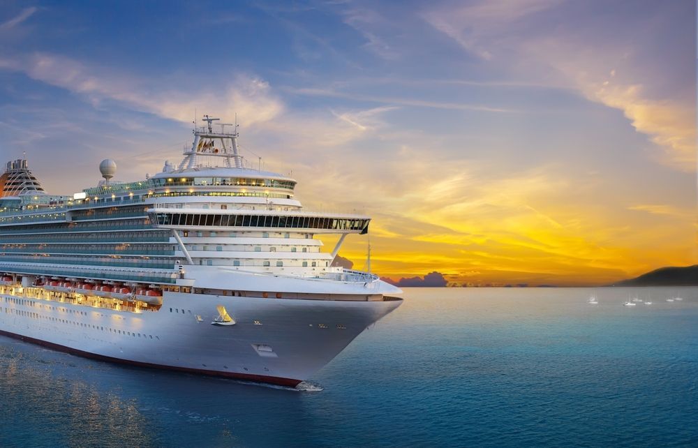 Large cruise ship docked at sunset, with calm blue water and orange sky in the background