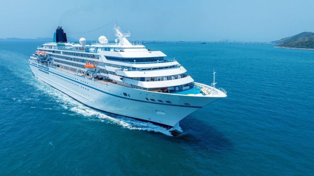 Large white cruise ship sailing on calm blue ocean near a coastline