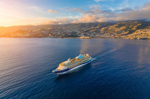 Cruise ship sailing on calm blue sea near a sunlit coastal town at sunset