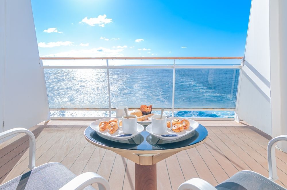 Balcony breakfast table with pastries and coffee overlooking a bright blue ocean