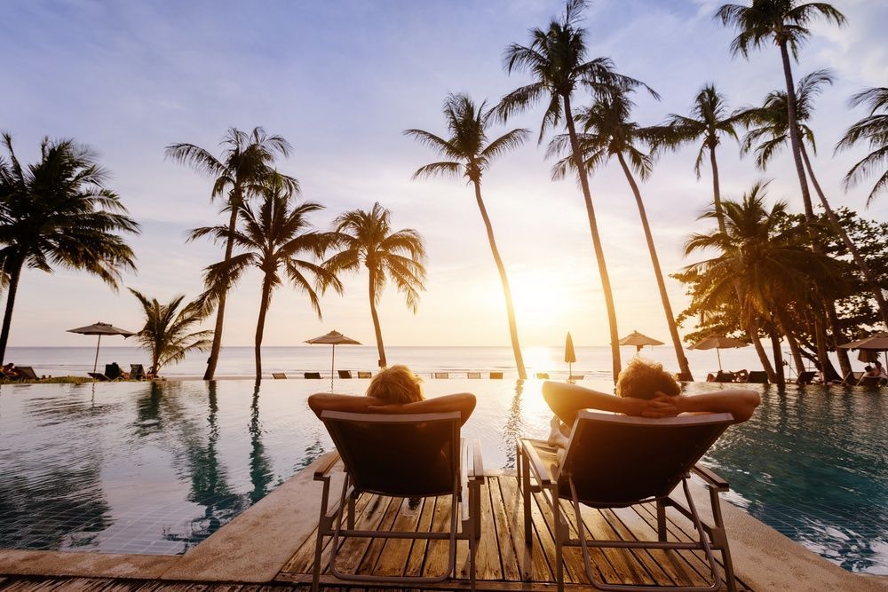 Tropical infinity pool at sunset with palm trees and lounge chairs overlooking the ocean